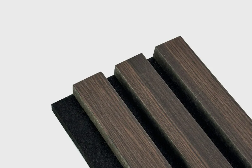 A close-up of three parallel, dark Stilj™ Sustainable Acoustic Wood Paneling slats mounted on a black base against a plain light gray background.