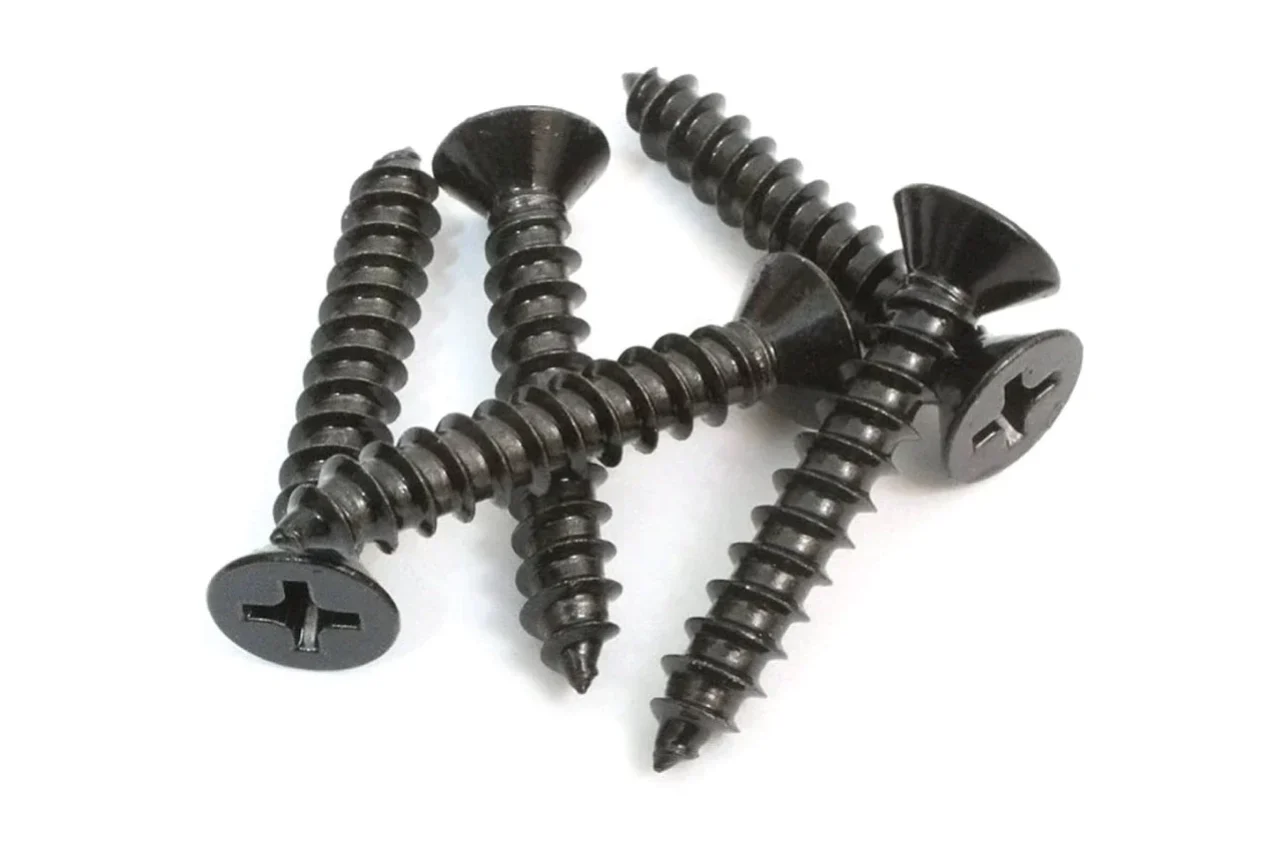 A small pile of black Accessories Phillips-head screws with pointed tips is scattered on a white background.